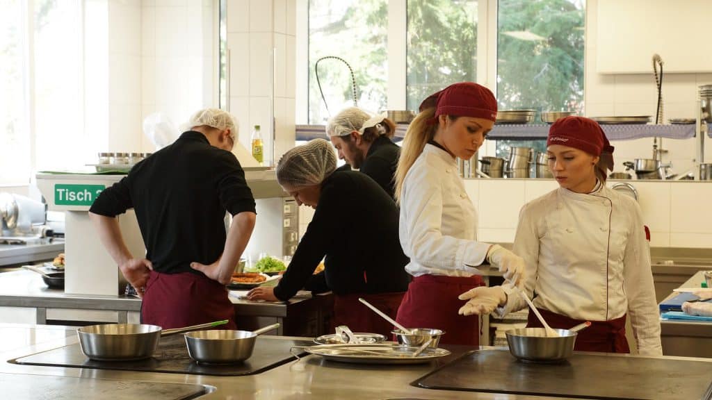 Junge Männer und Frauen als Auszubildende in der Gastronomie bei der Arbeit.