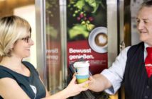 Deutsche Bahn stellt auf Fairtrade-Kaffee um Eine DB-Servicekraft überreicht einer Reisenden einen Fairtrade-Kaffee
